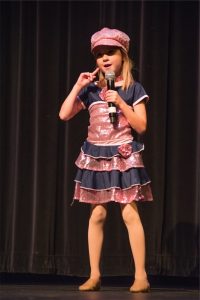 A little girl in a pink dress holding a microphone.