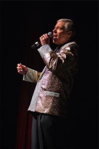 A man in a silver suit singing into a microphone.