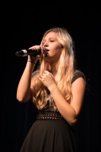 A girl in a black dress singing into a microphone.