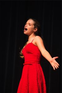 A girl in a red dress singing on stage.