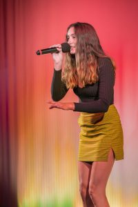 A woman in a yellow skirt singing into a microphone.