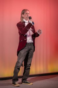 A man in a red jacket holding a microphone.