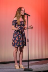 A girl in a floral dress singing into a microphone.