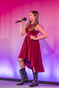 A girl in a red dress singing into a microphone.
