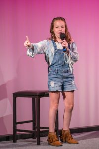 A girl in overalls is holding a microphone.