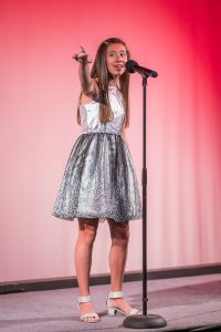 A girl in a silver dress singing into a microphone.