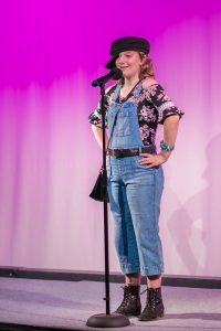 A girl wearing overalls and a hat on stage.