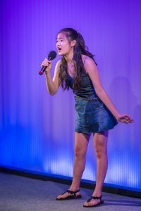 A girl in a blue dress singing into a microphone.