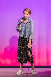 A girl in a polka dot dress is singing into a microphone.