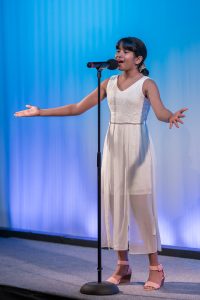 A girl in a white dress singing into a microphone.