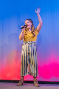 A girl singing on stage with a microphone.