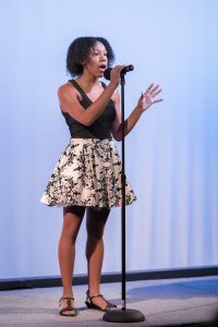 A young woman singing into a microphone.