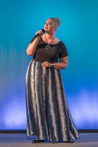 A woman in a blue and black skirt singing into a microphone.