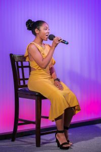 A woman in a yellow dress singing into a microphone.