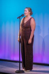 A woman in a brown dress singing into a microphone.