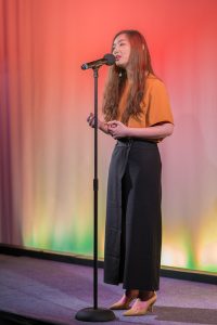 A woman singing into a microphone on stage.