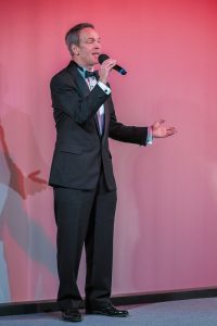 A man in a tuxedo singing into a microphone.