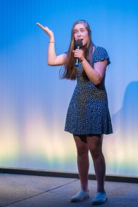 A girl is holding a microphone in front of a stage.