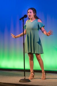 A girl in a blue dress singing into a microphone.