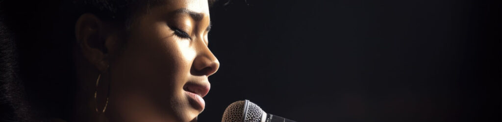 Close-up of a woman singing into a microphone with dramatic lighting.