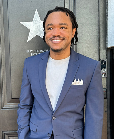 Smiling man in a blue suit standing in front of a wall with a star plaque.