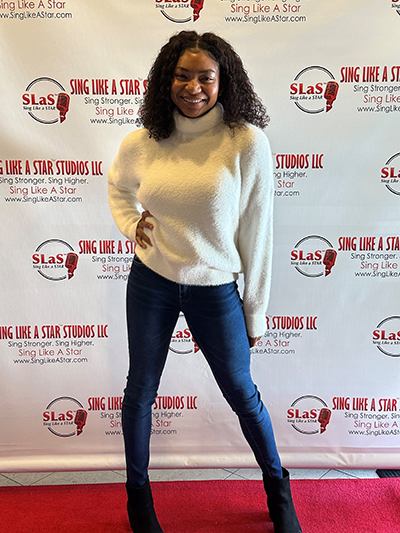 A woman smiling and posing in front of a sing like a star studios step-and-repeat banner.